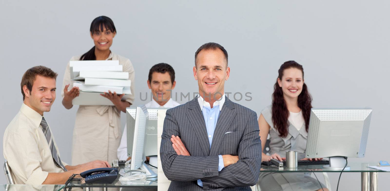 Self-assured manager with folded arms with his team in the background