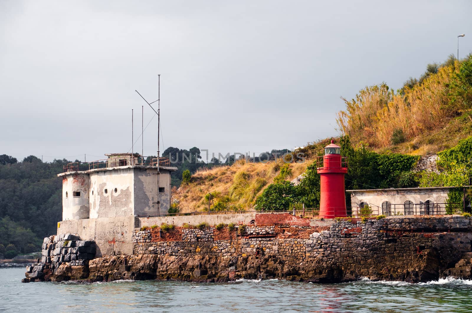 small red lighthouse on a stony shore in italy