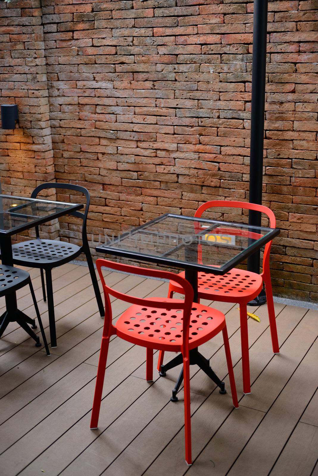 The metal red modern chair next to brick wall.