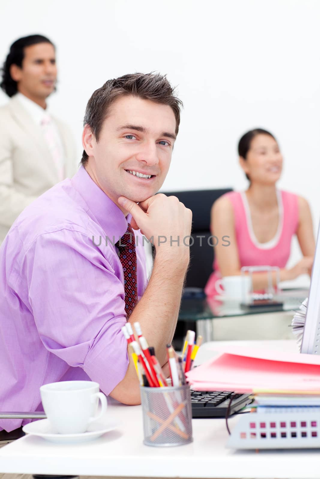 Attractive businessman smiling at the camera with his colleagues in the background