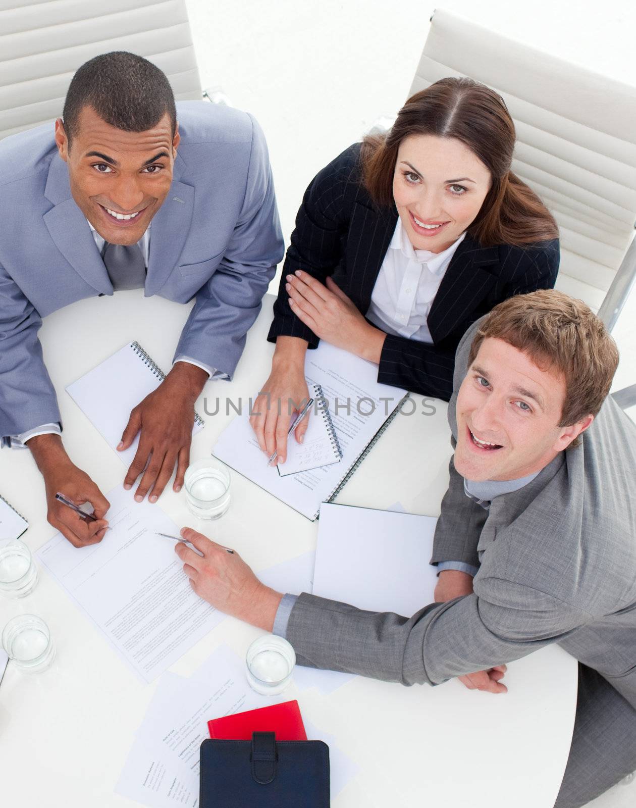 High angle of three multi-ethnic colleagues smiling at the camera in a meeting