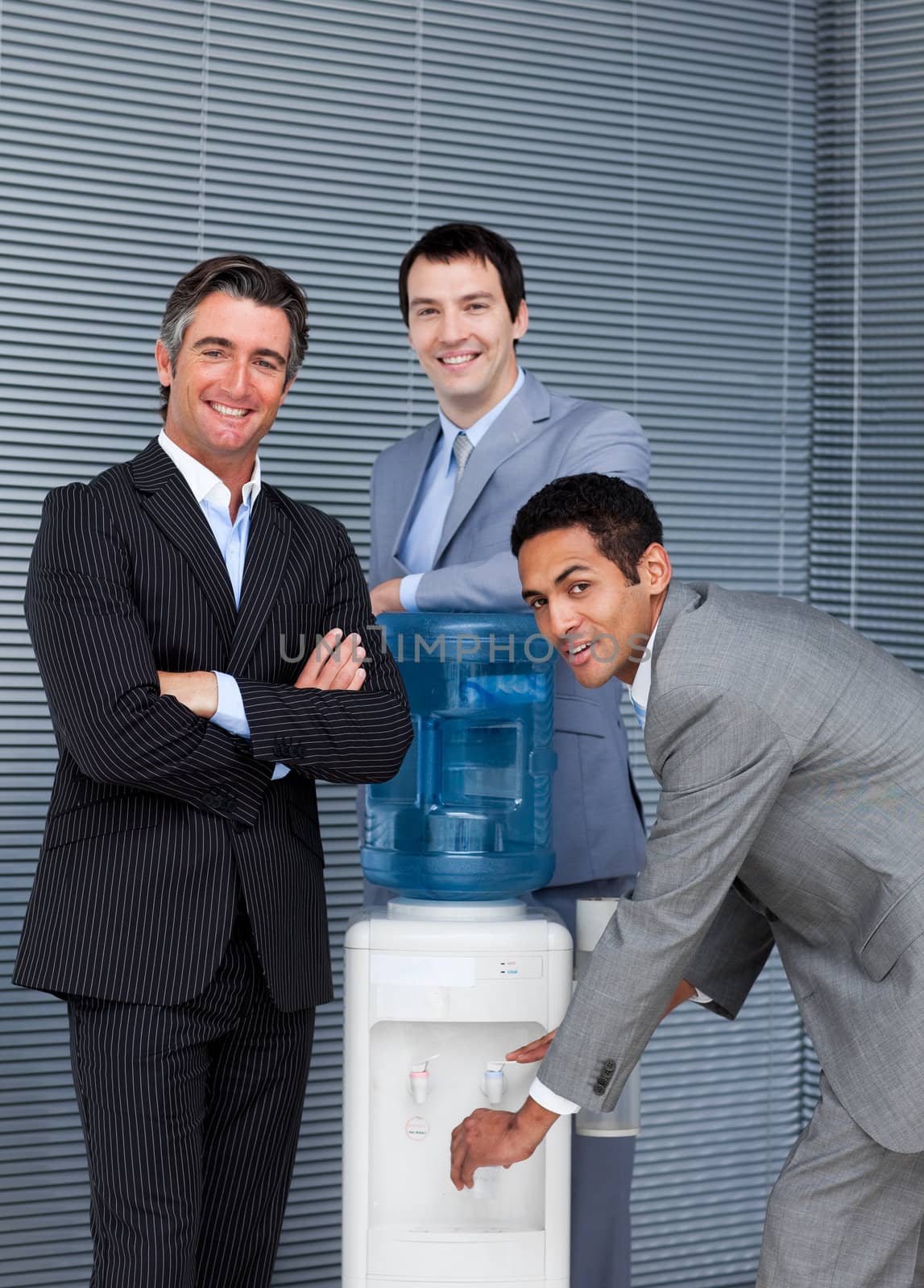 Portrait of a business team filling cup from water cooler in the office