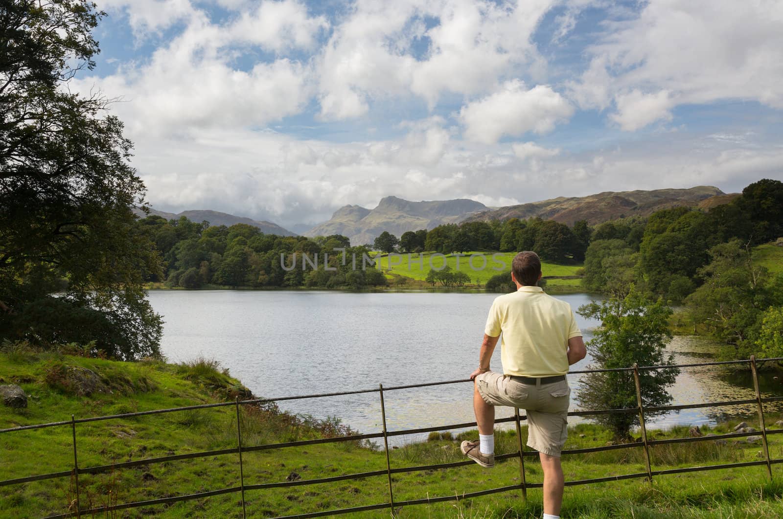 Sun illuminating Langdale Pikes with Loughrigg Tarn in foreground and hiker