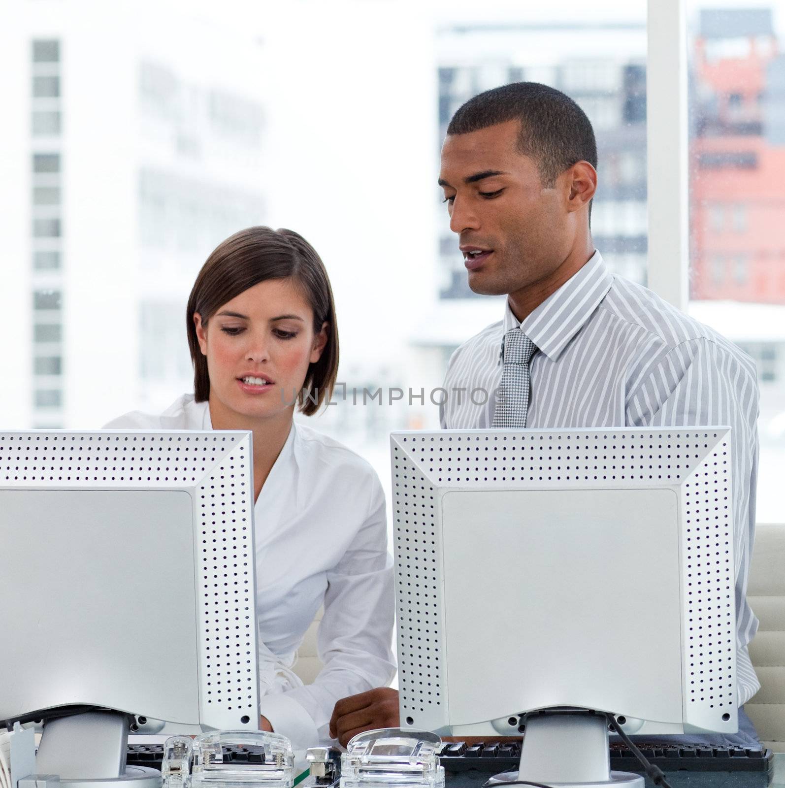 Two business people helping each other with their computers in the office