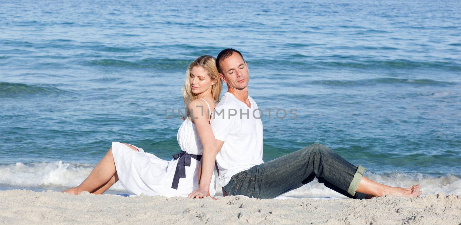 Romantic couple sitting on the sand  by Wavebreakmedia
