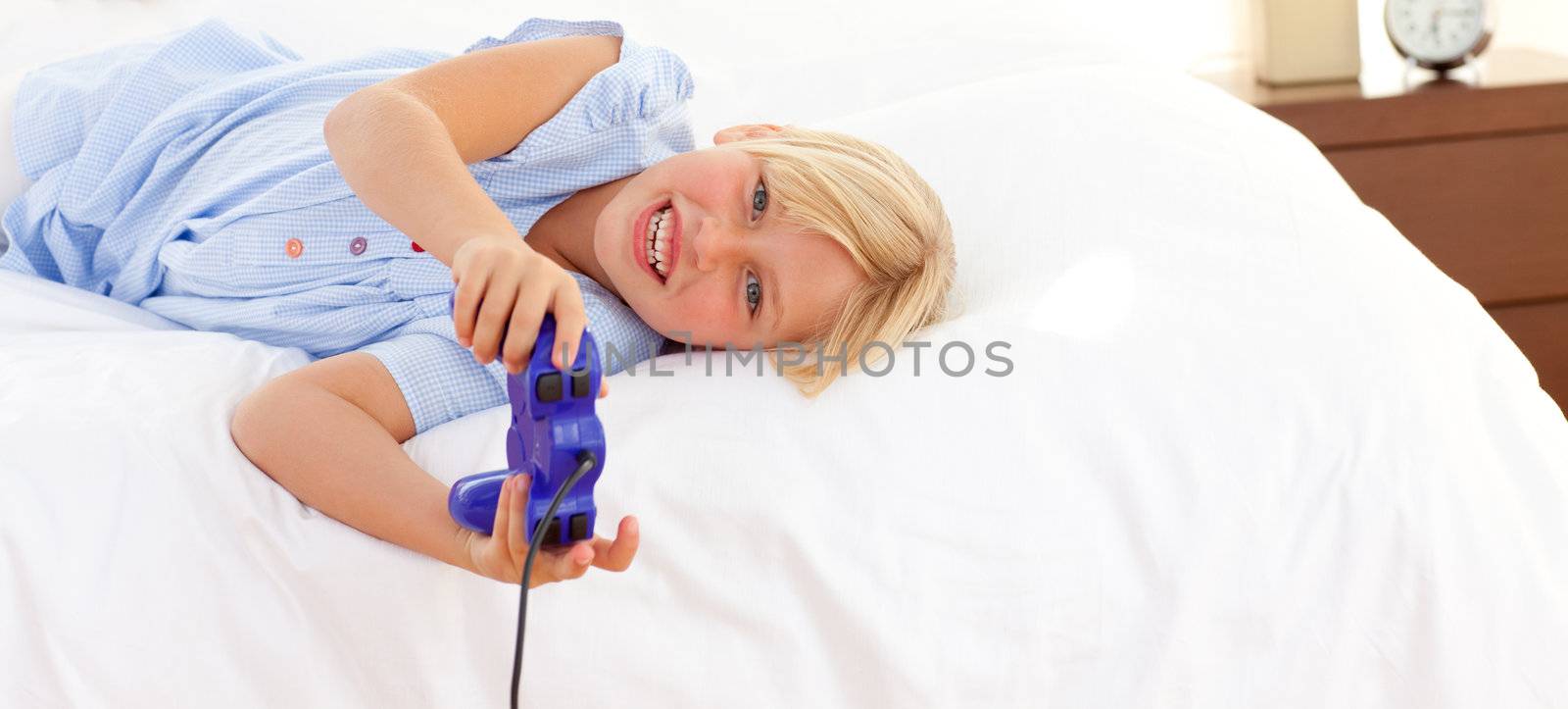 Adorable little girl playing video game lying on bed