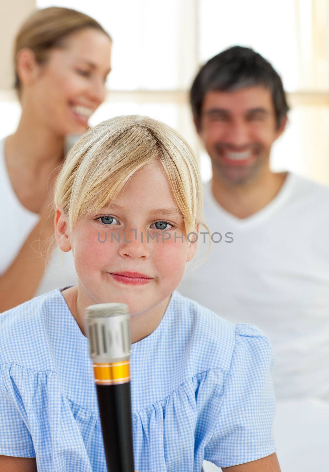 Blond child singing with a microphone sitting on her parent's bed