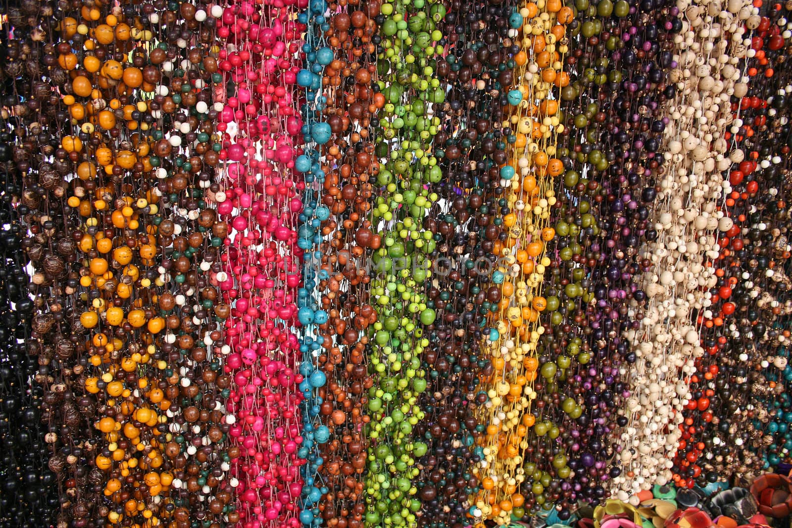 Strings of colorful carved and dyed tagua nut beads hanging for sale at the outdoor craft market in Otavalo, Ecuador