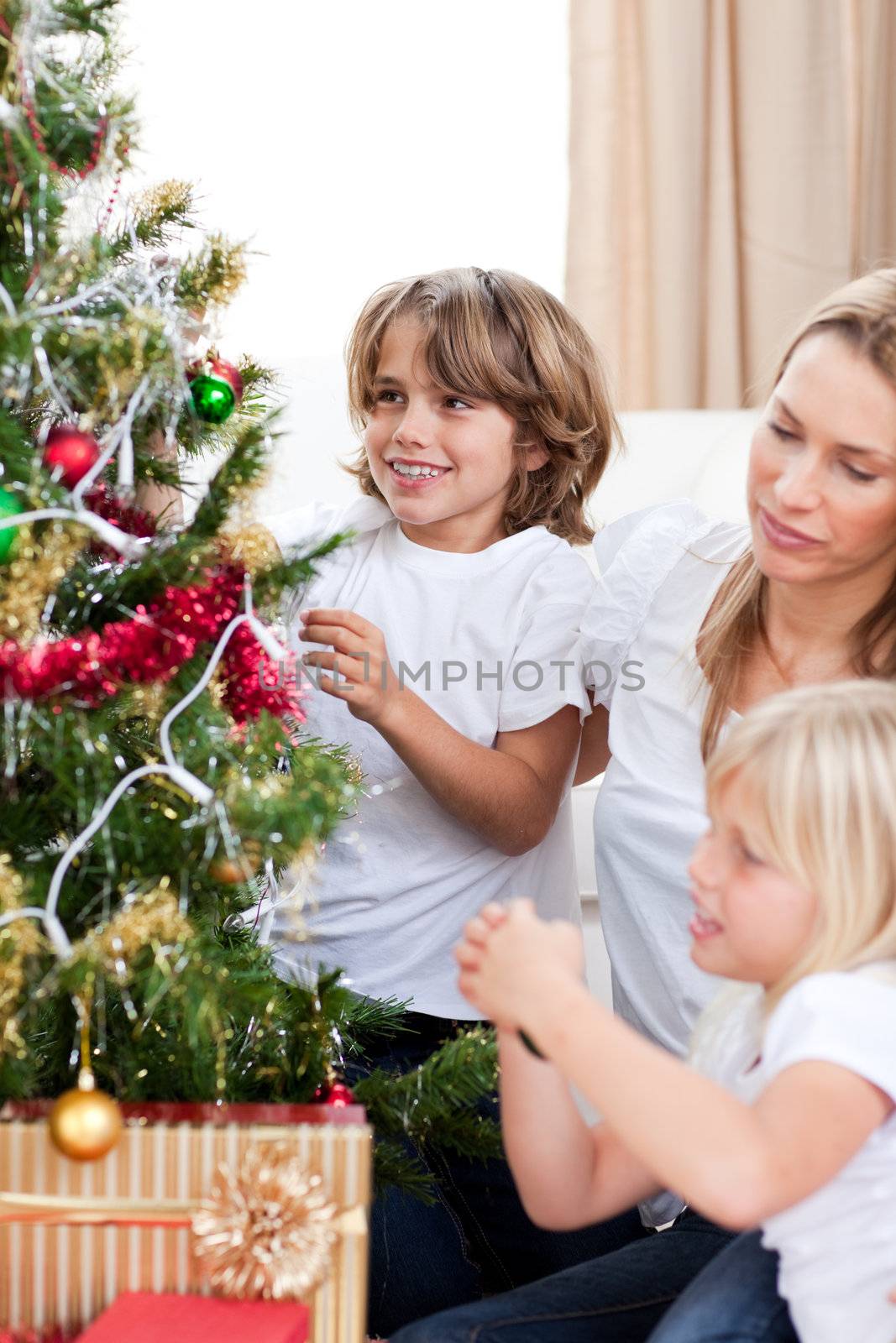 Happy mother and her children hanging Christmas decorations at home