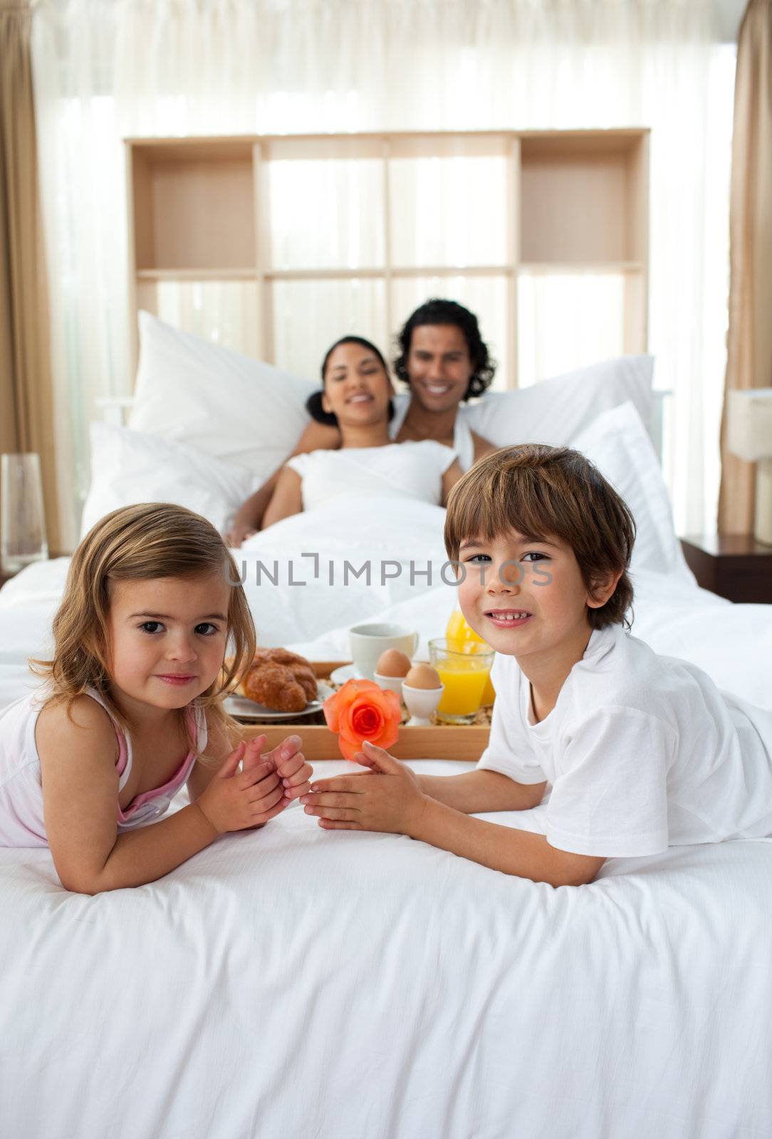 Siblings having breakfast with their parents lying on the bed
