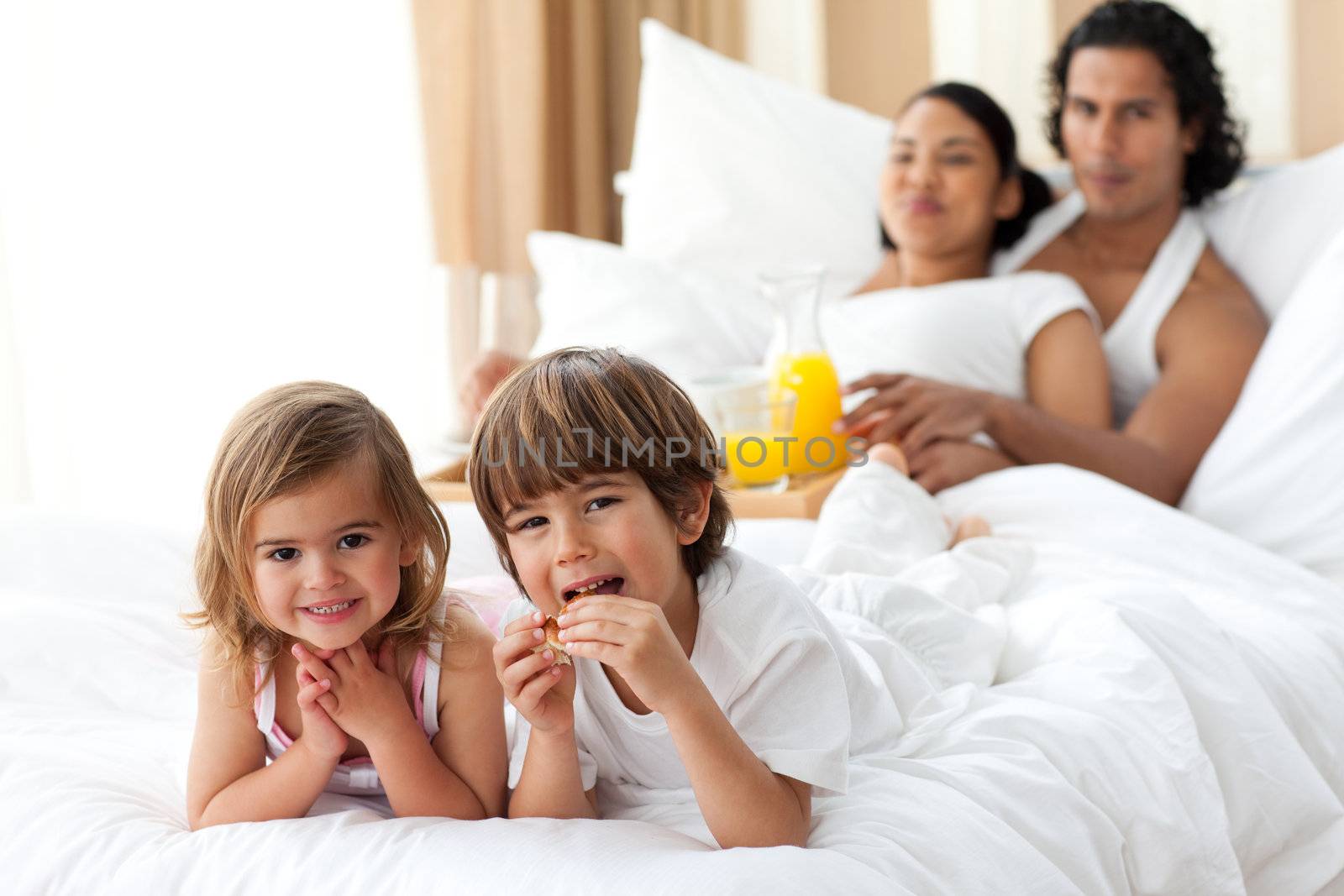 Happy siblings having breakfast with their parents lying on the bed