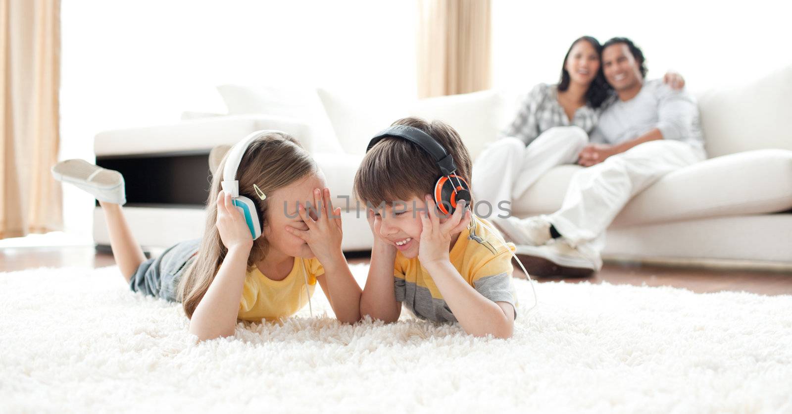 Laughing children listening music with headphones lying on the floor