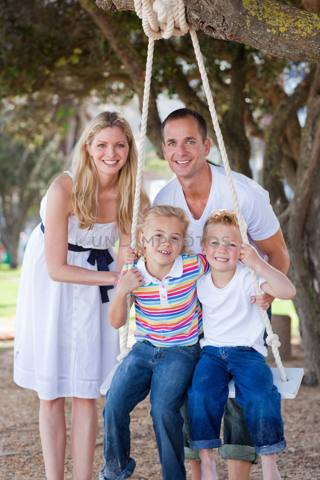 Attentive parents pushing their children on a swing in a park