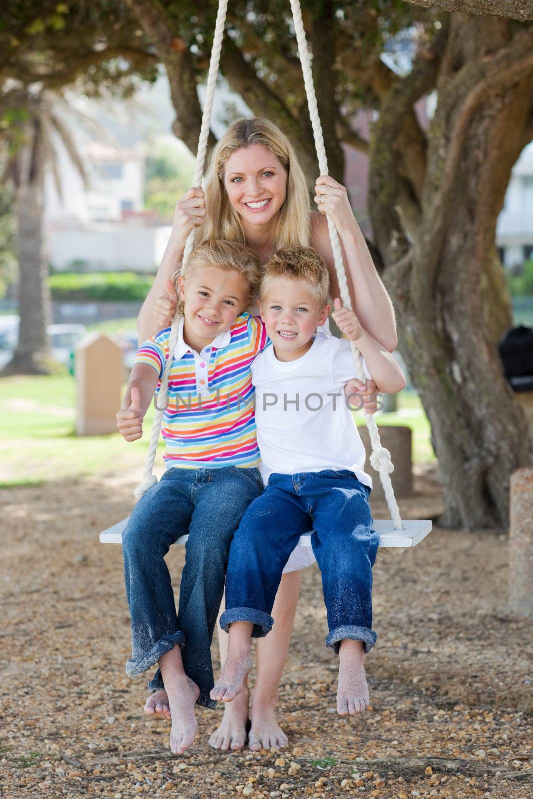 Smiling mother and her children swinging in a park