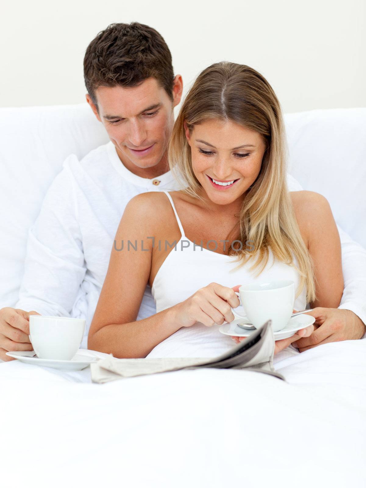 Romantic couple reading a newspaper and drinking coffee lying on their bed