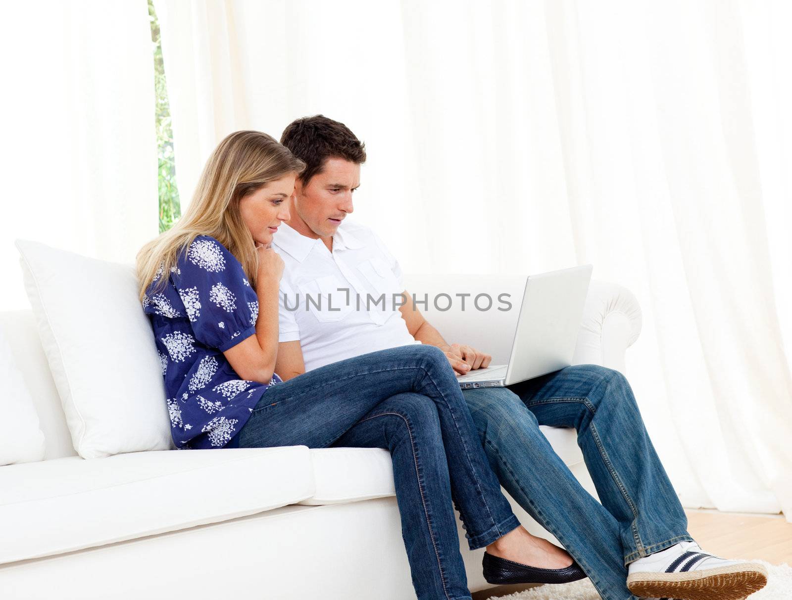 Romantic couple using a laptop sitting on sofa at home