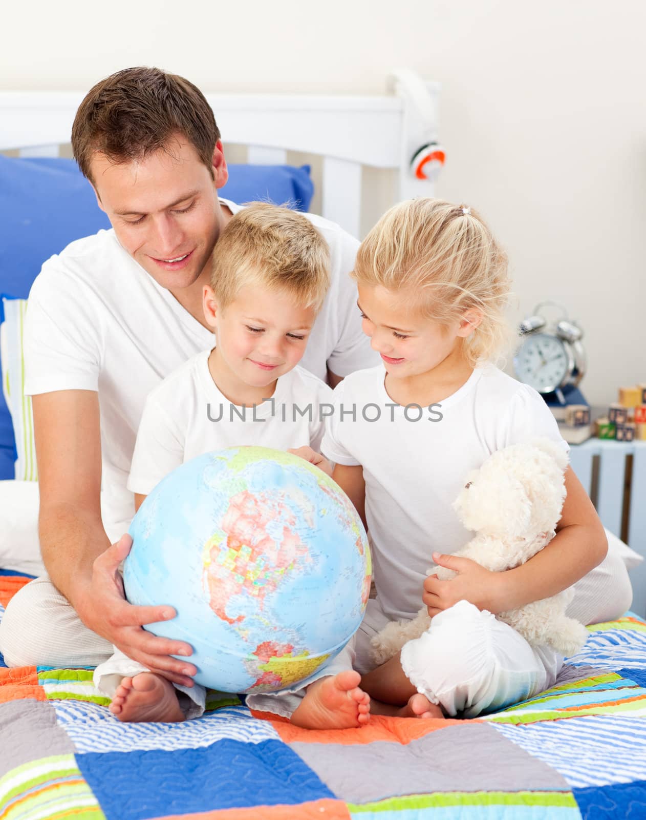 Jolly father and his children holding a terretrial globe sitting on a bed