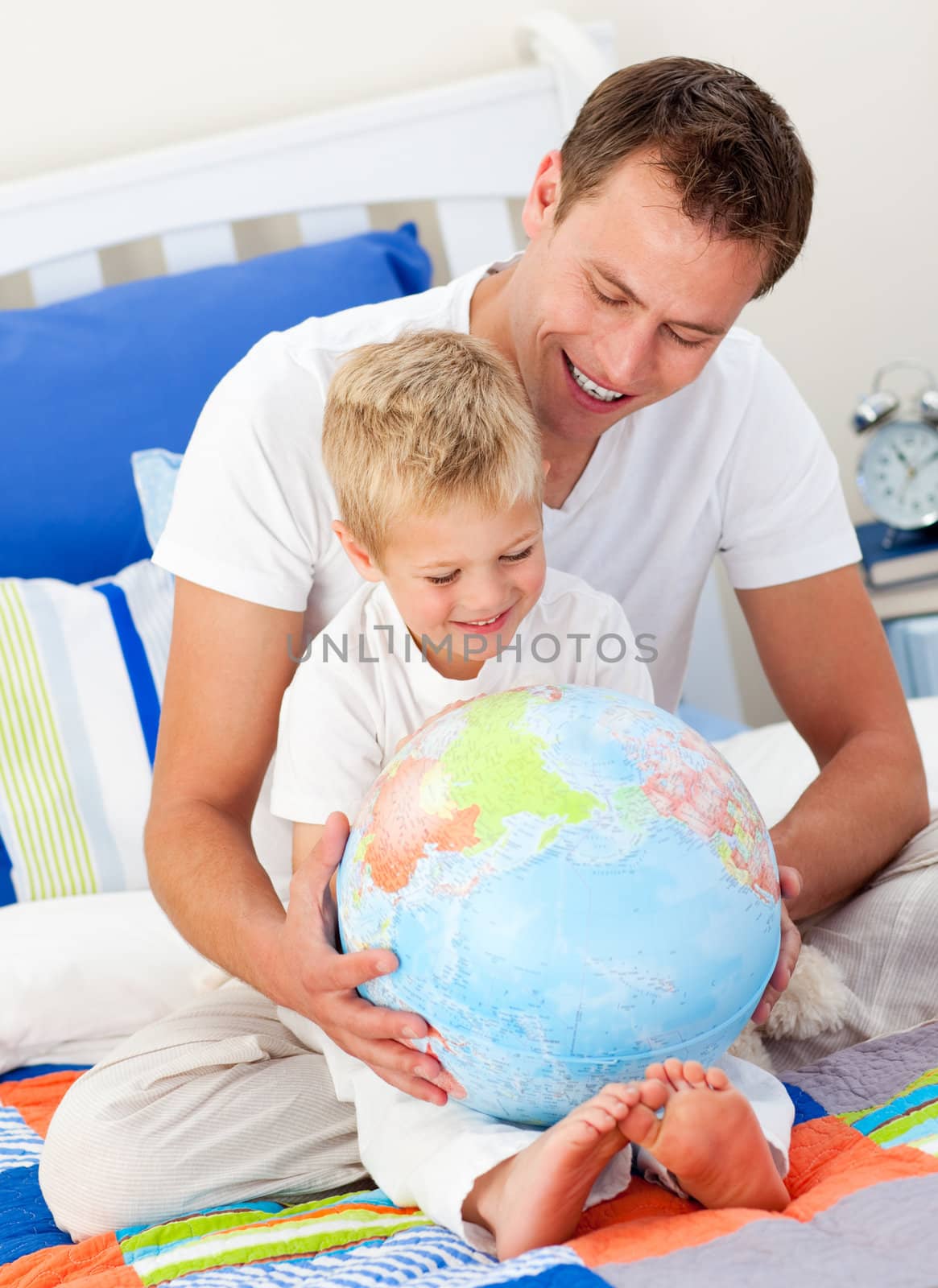 Merry father and his son looking at a terrestrial globe sitting on bed