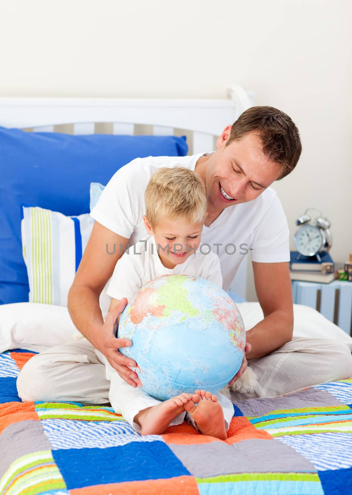 Enthusiastic father and his son looking at a terrestrial globe sitting on bed