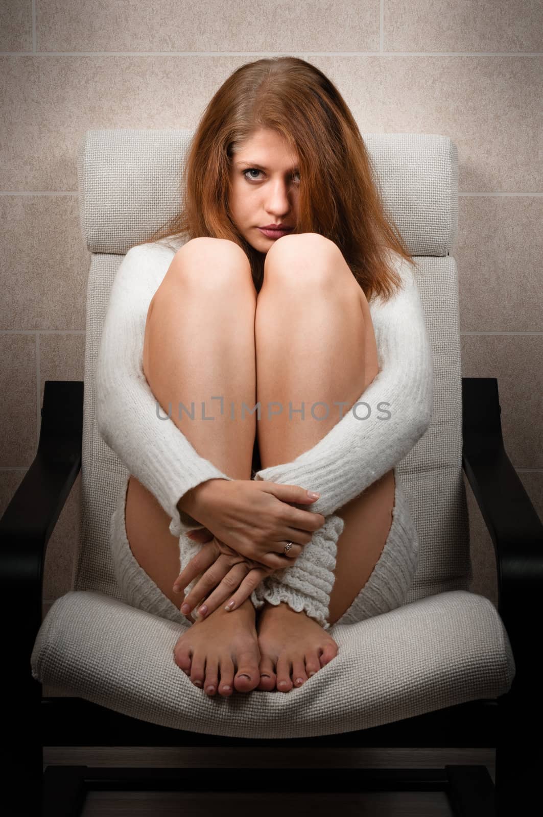 Girl sitting on chair in room and hugs her legs