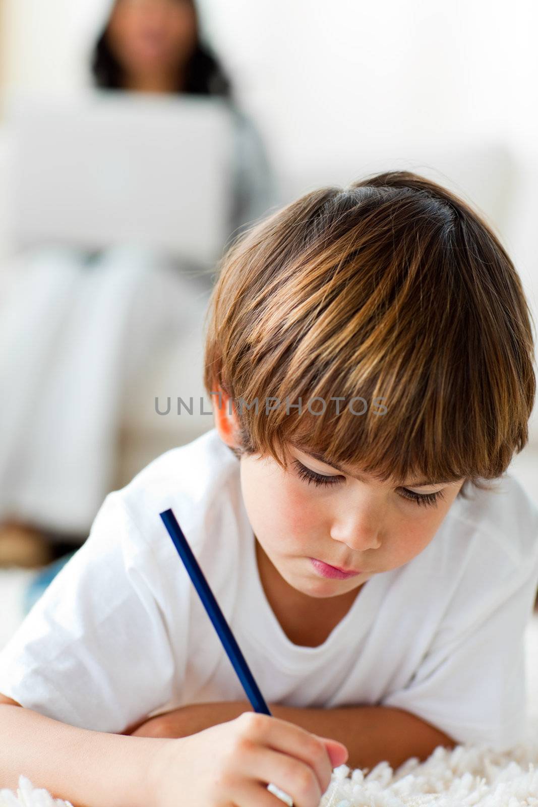 Concentrated little boy drawing lying on the floor  by Wavebreakmedia