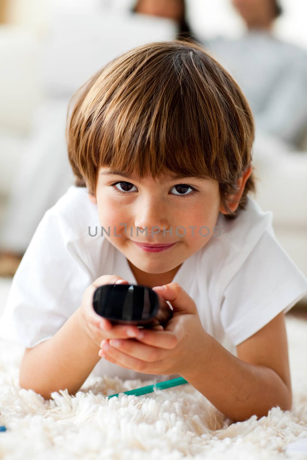 Smiling little boy holding a remote lying on the floor in the living-room