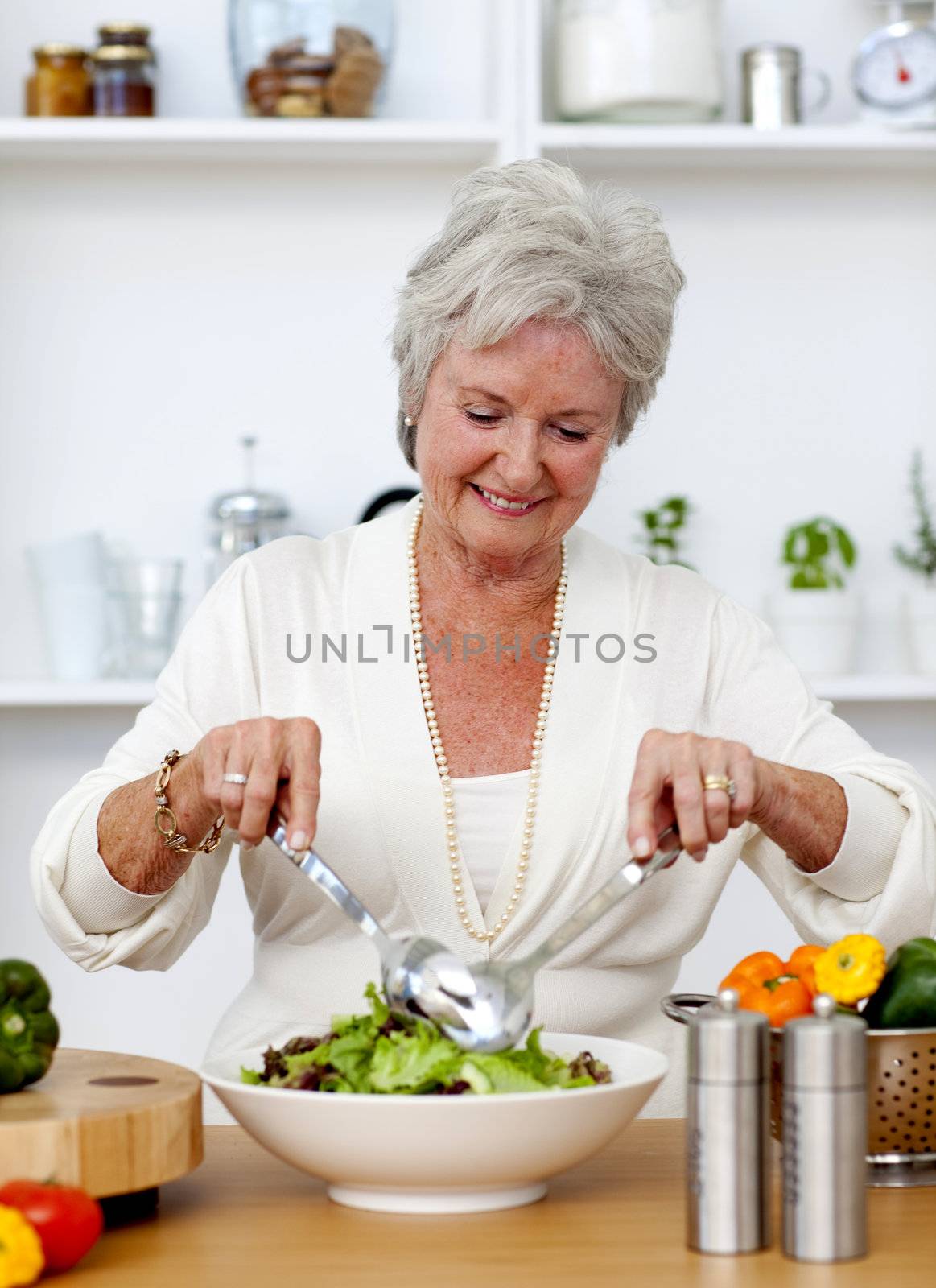 Happy senior woman cooking a salad in the kitchen