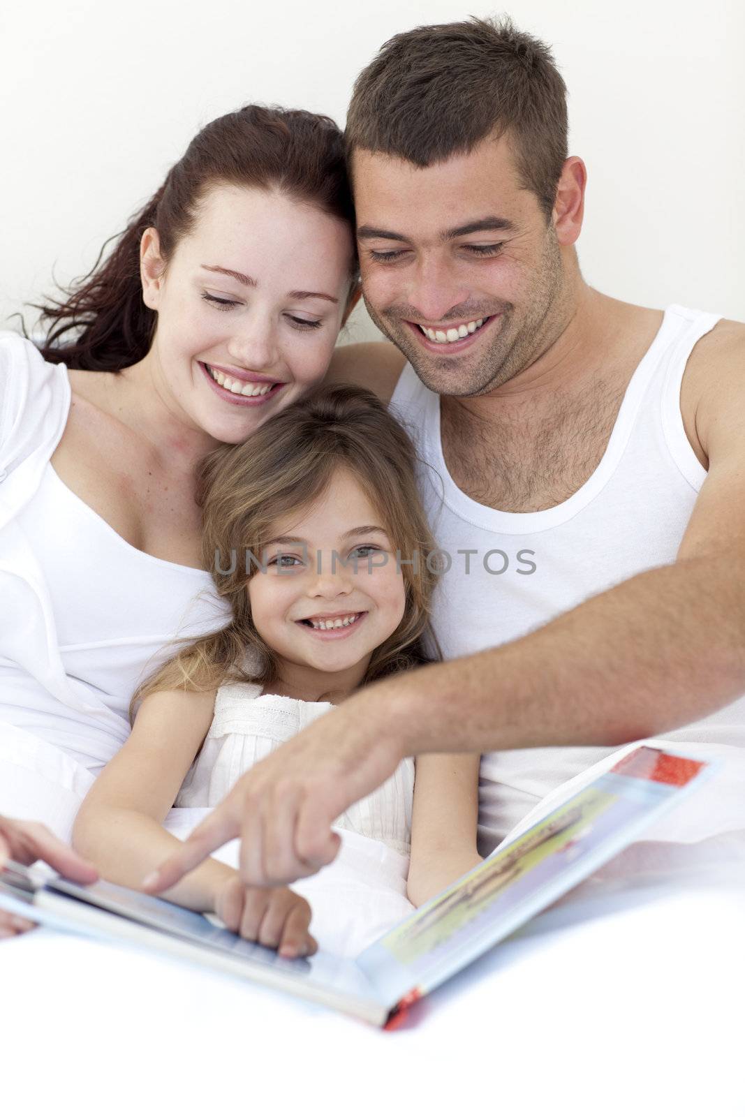 Portrait of a girl reading with her parents in bed by Wavebreakmedia