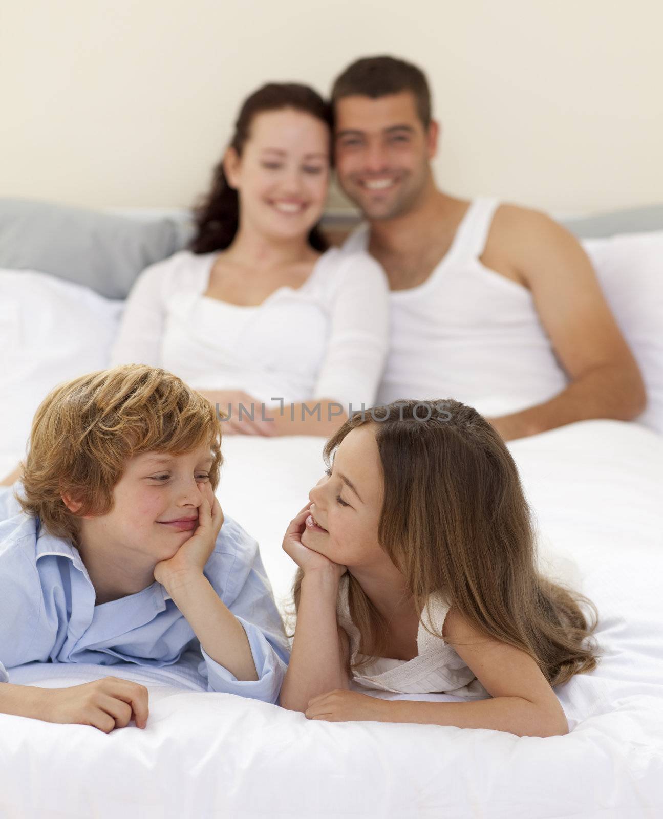 Little brother and sister looking at each other in bed with her parents