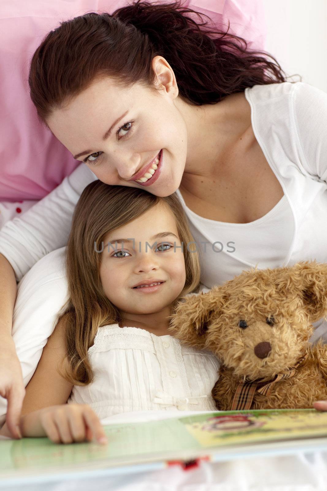 Beautiful mother and daughter reading a book together in bed