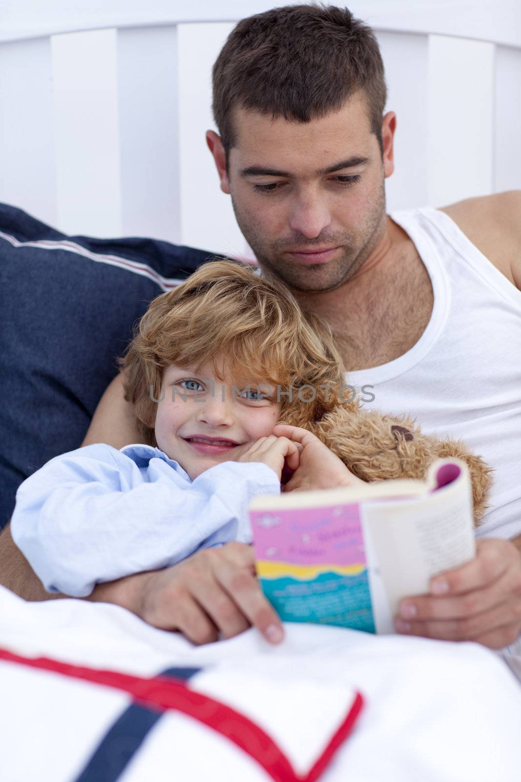 Little son reading with his father a book in bed