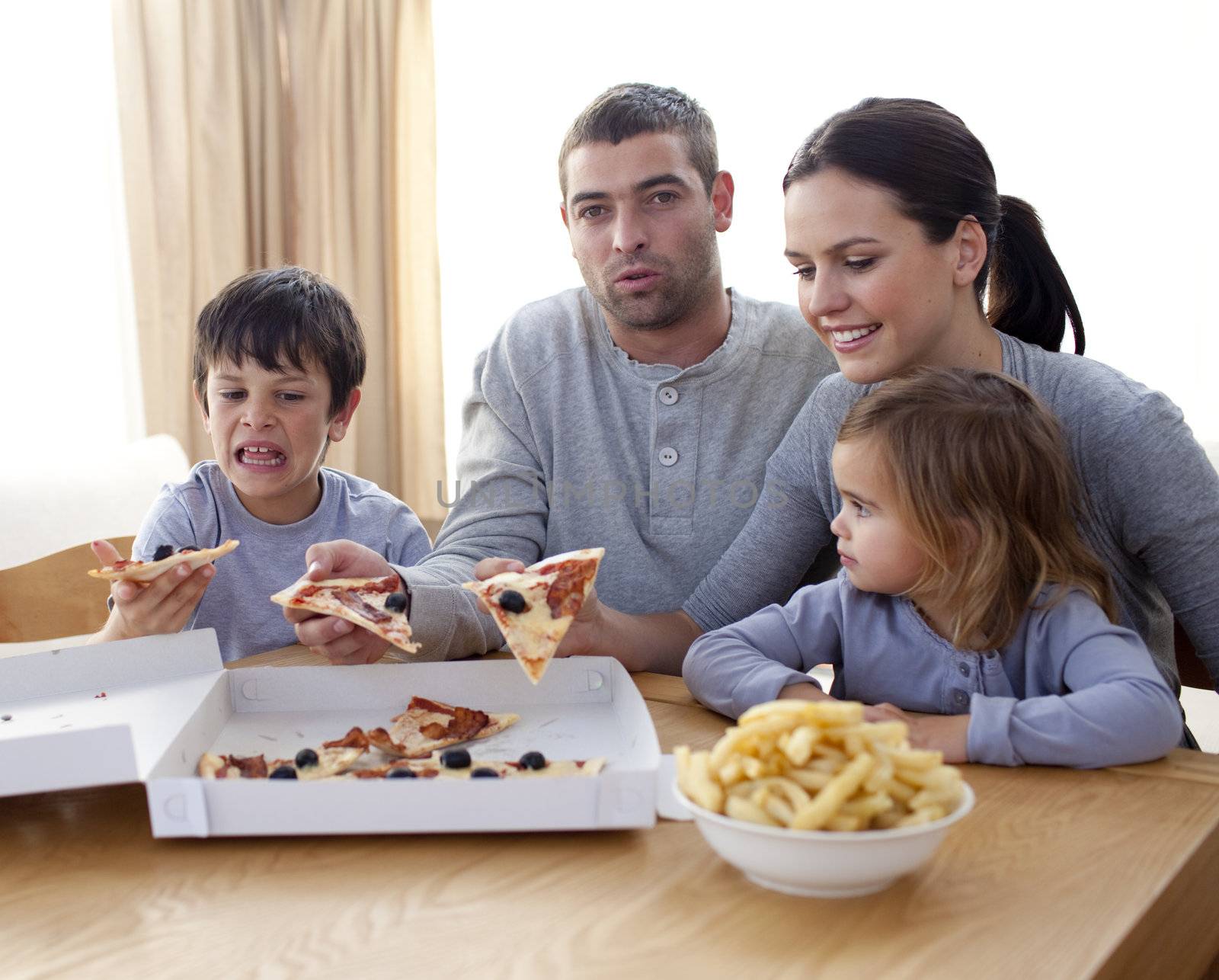 Parents and children eating pizza and fries on a sofa