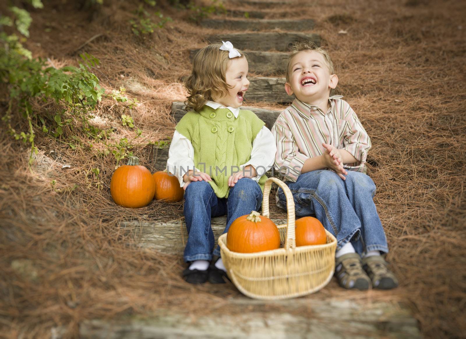 Cute Young Brother and Sister Children Sitting on Wood Steps Laughing with Pumpkins in a Basket.