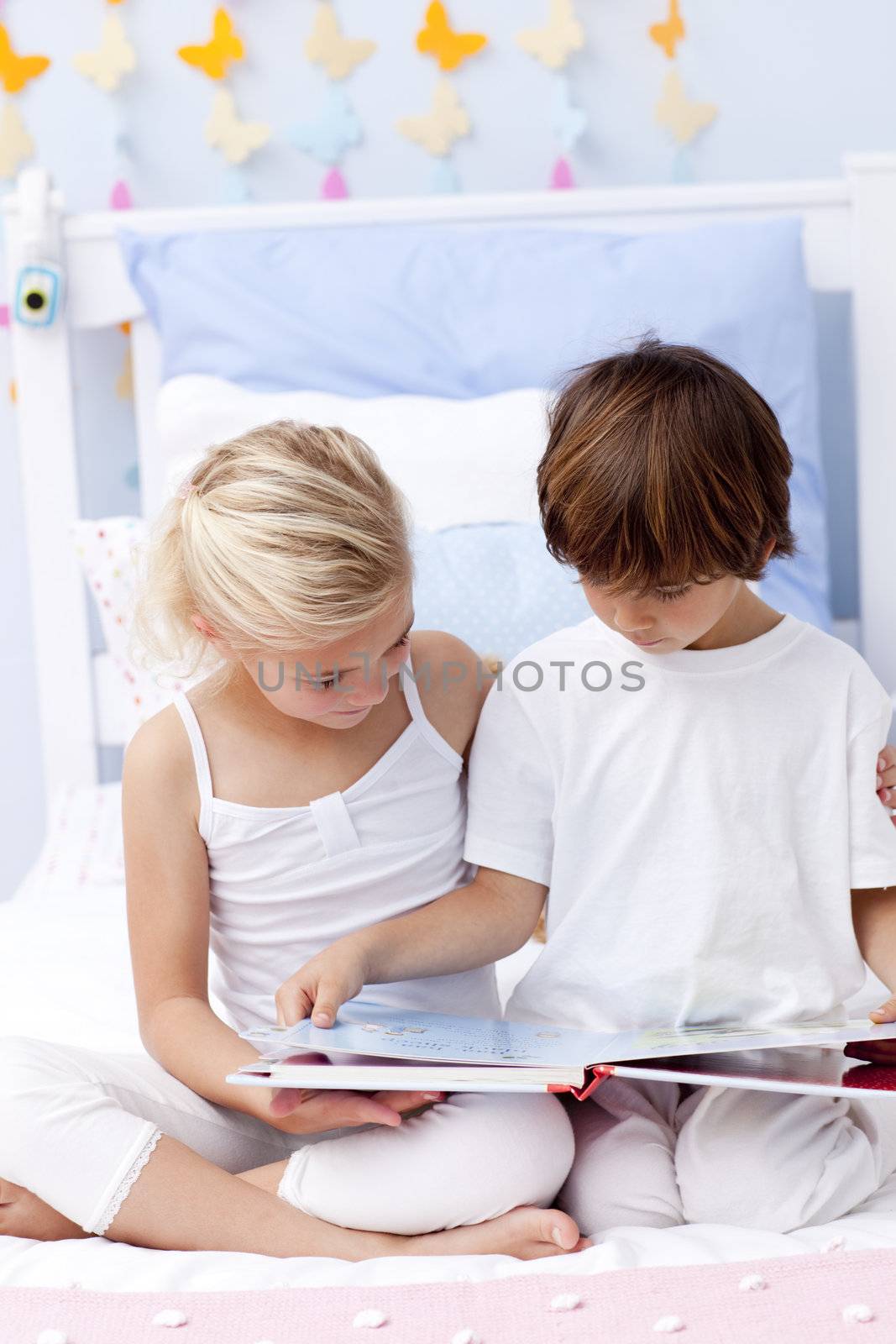 Little brother and sister reading a book in bedroom