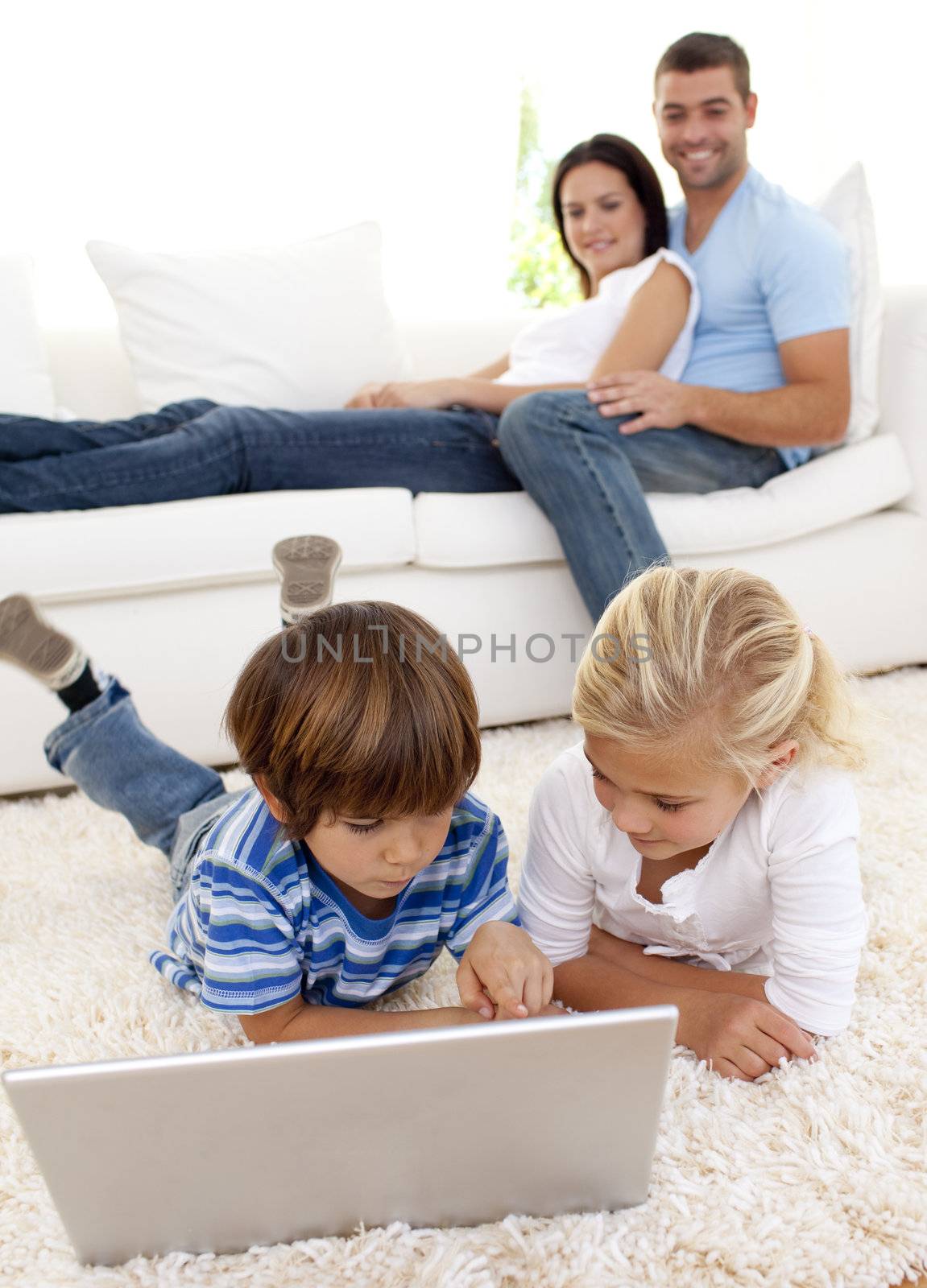 Children using a laptop on floor and parents lying on sofa