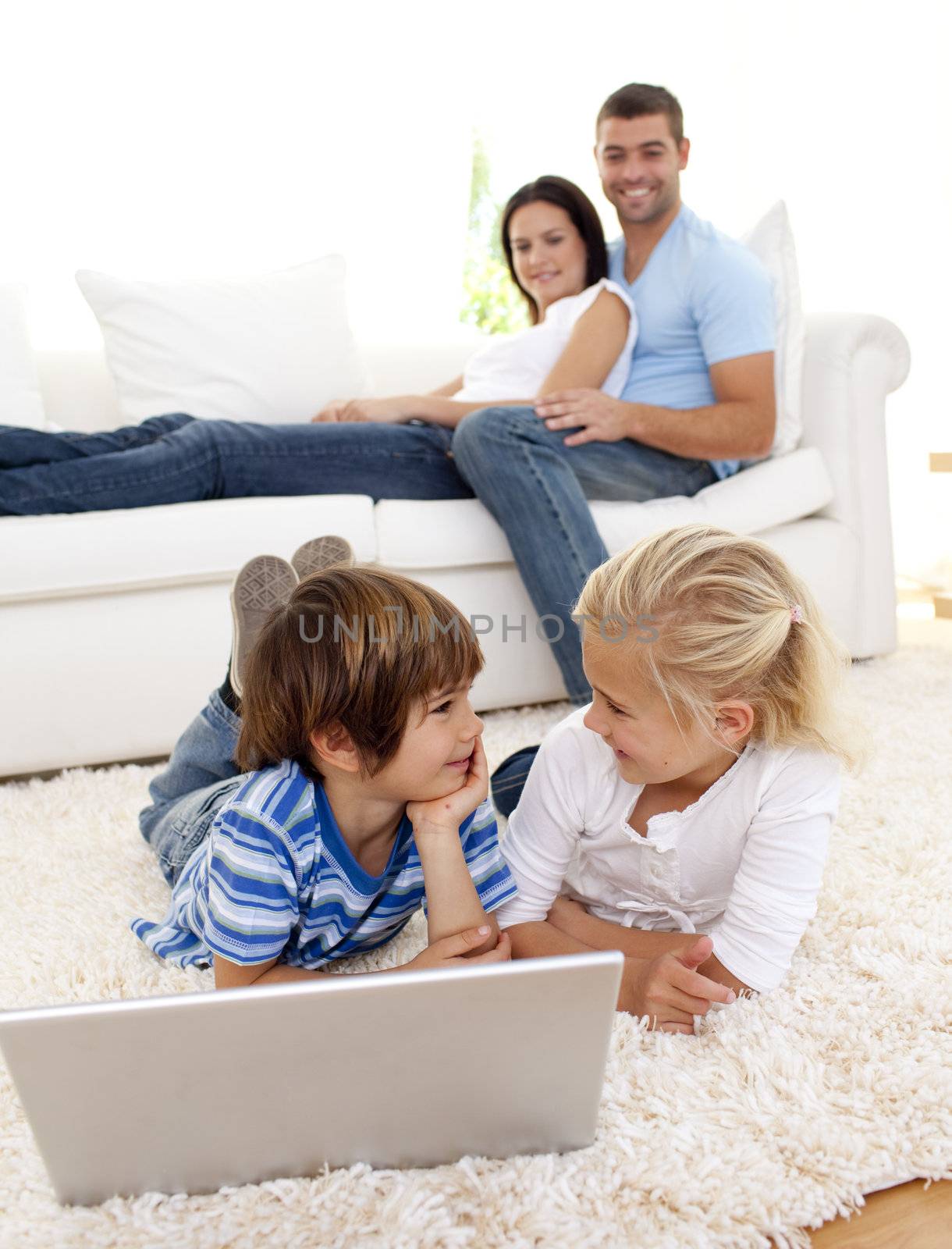 Friends using a laptop on floor and couple lying on sofa