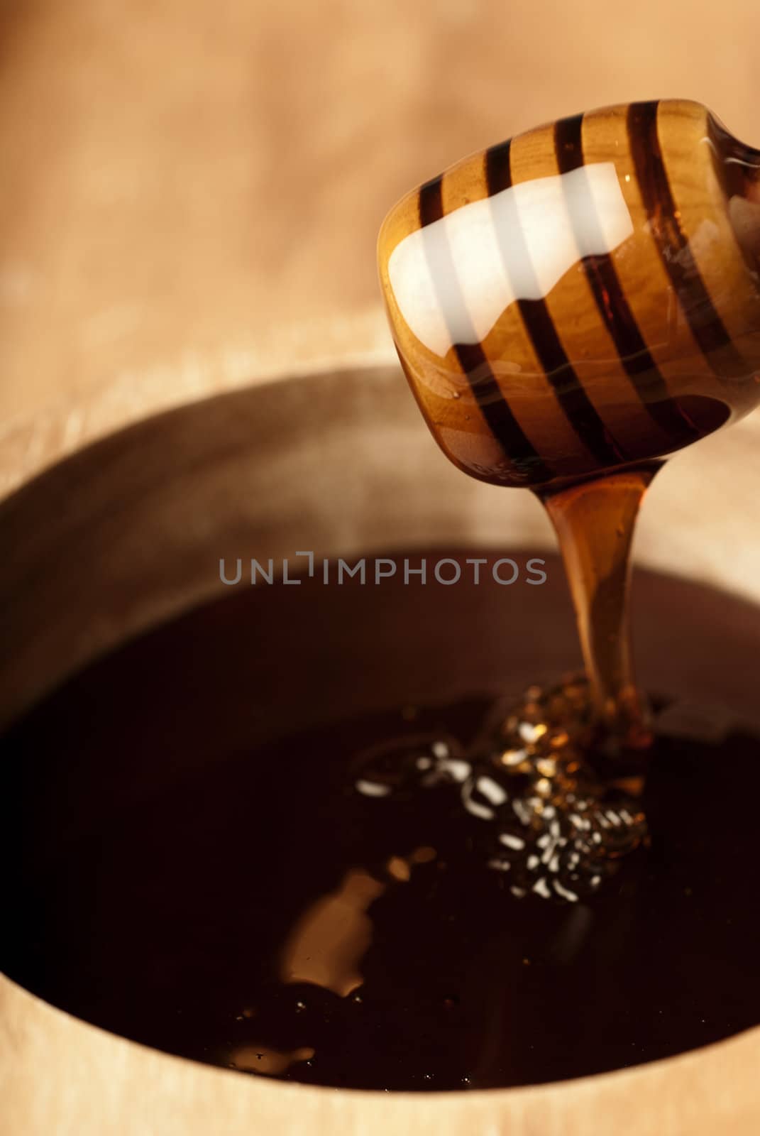 Dense honey in a wooden bowl dripping from a dripper