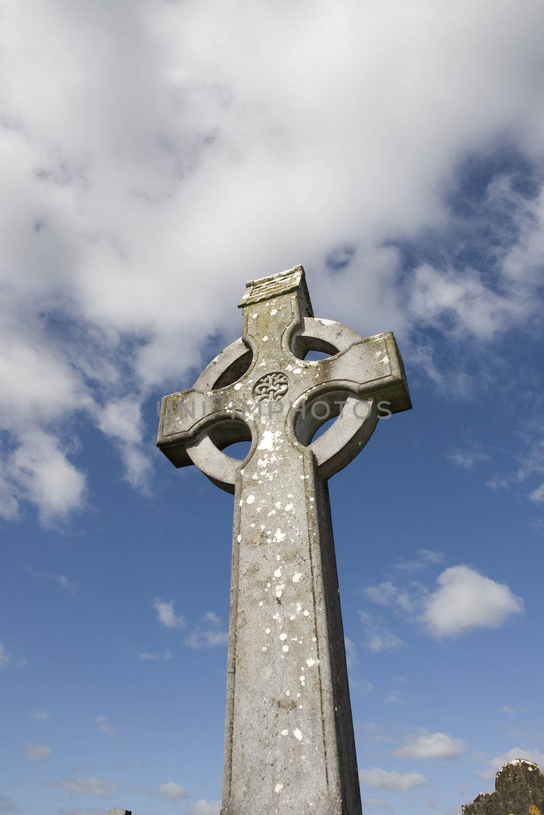 old celtic cross in an irish graveyard with blue cloudy sky