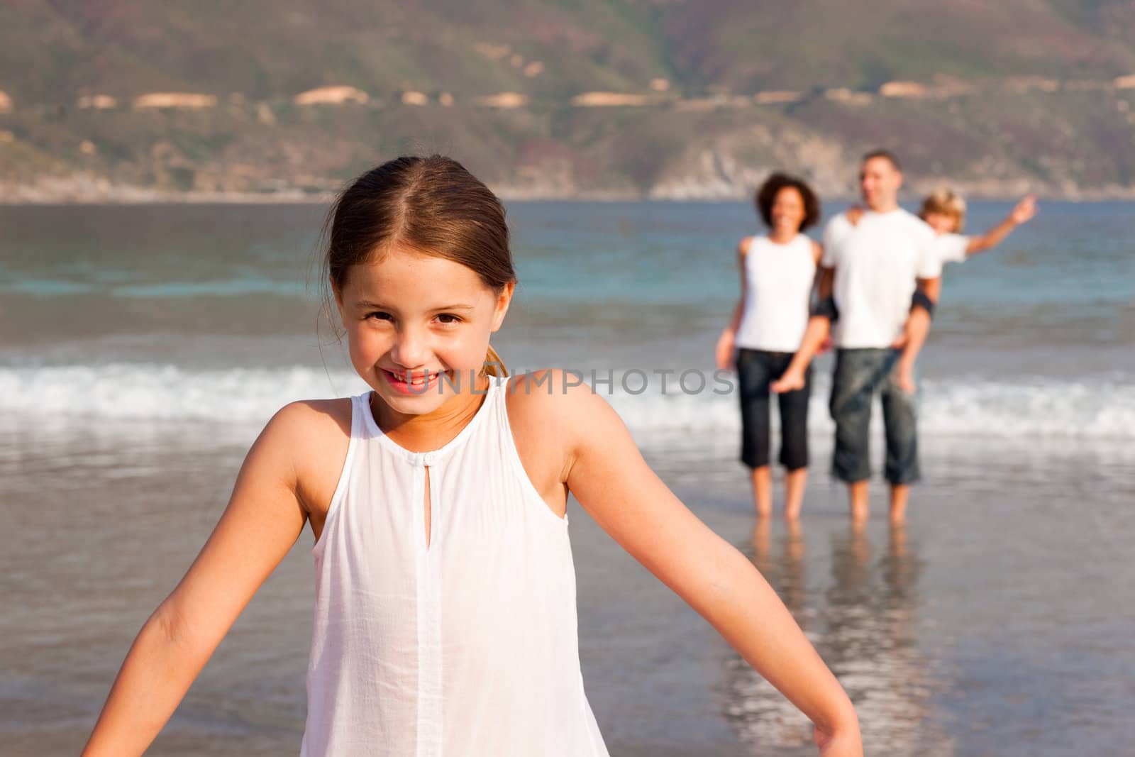 Little girl on a beach with her parents and her brother in background by Wavebreakmedia