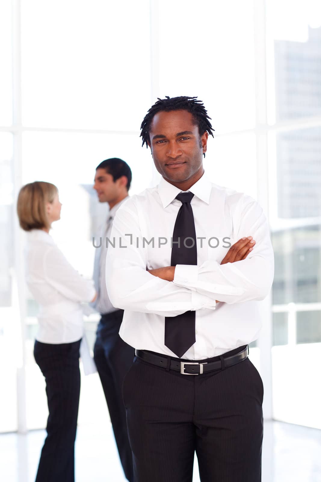 Smiling African businessman with folded arms with his team in the background