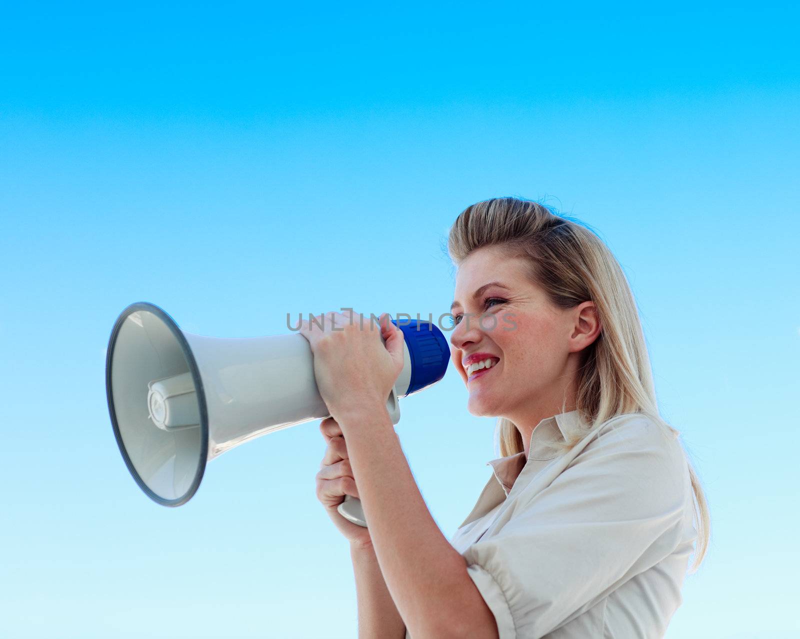 Businesswoman shouting through megaphone outdoors against blue sky