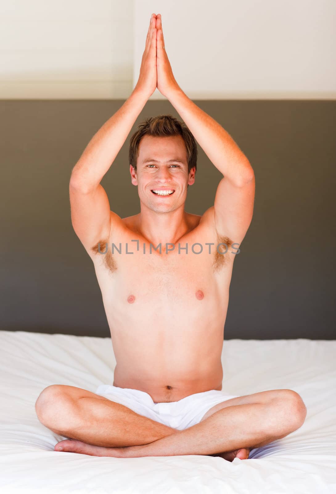 Handsome young man meditating on bed smiling at the camera