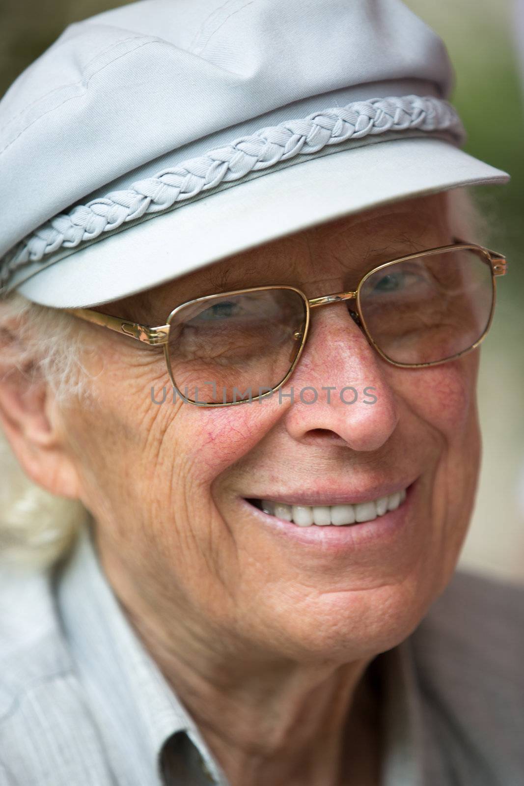 Senior man smiling at camera with his hat and glasses.