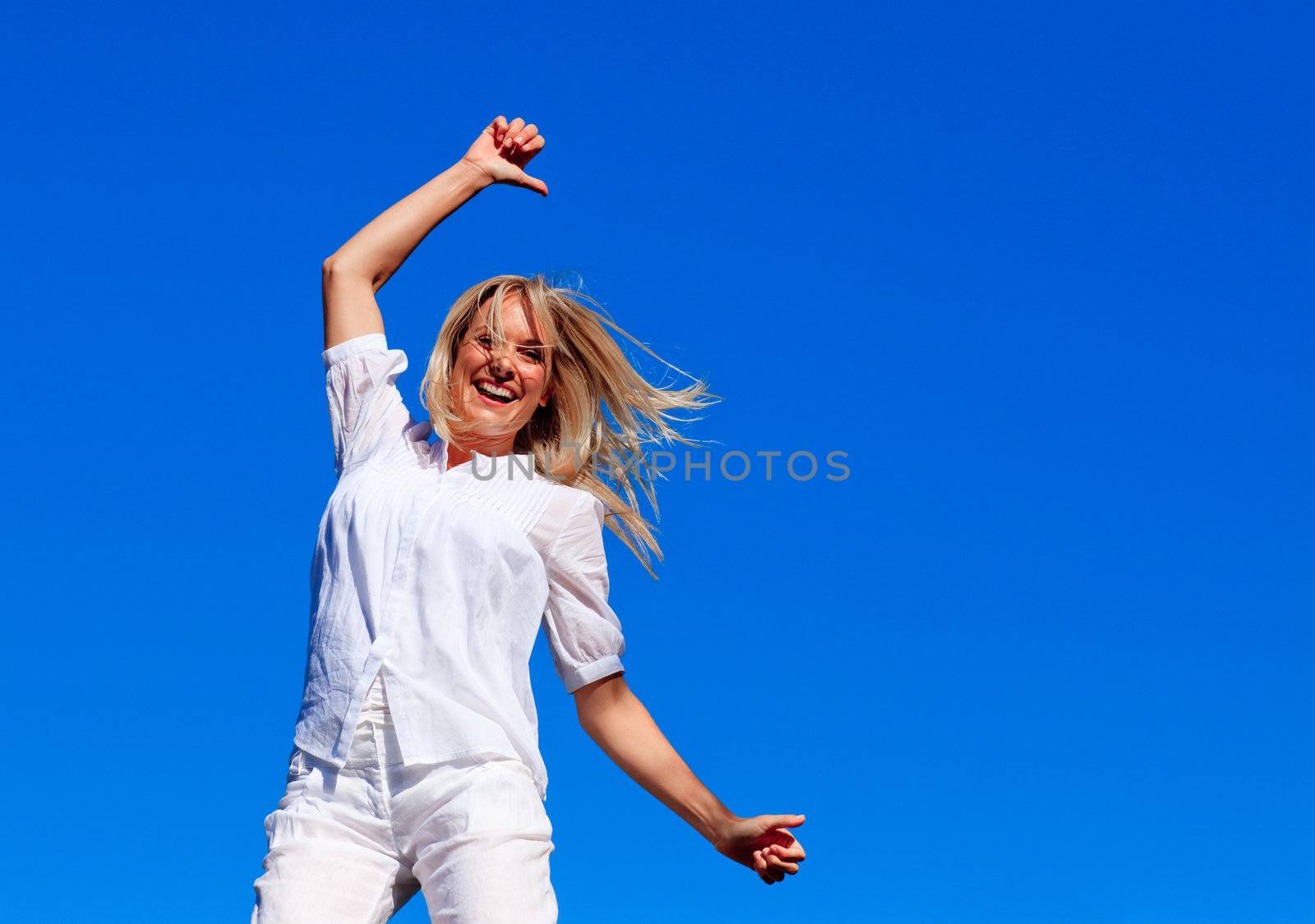 Smiling woman jumping outdoors against blue sky