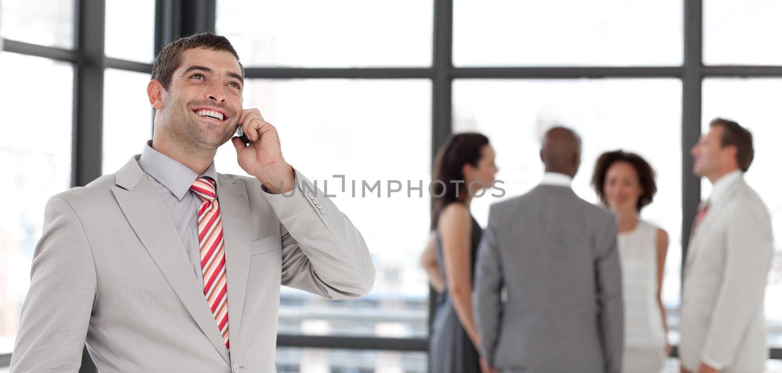 Charismatic businessman on phone in office with his team in the background 