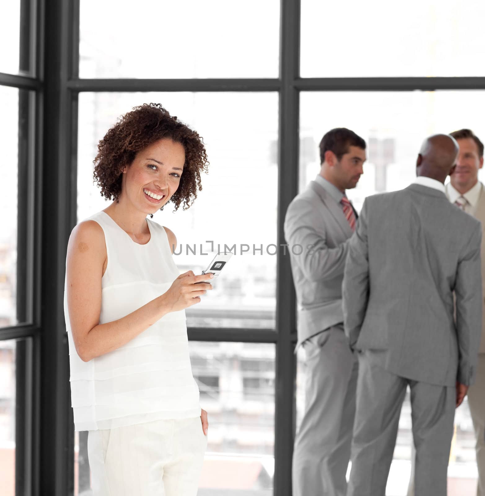 Cute businesswoman on phone in office with her team in the background