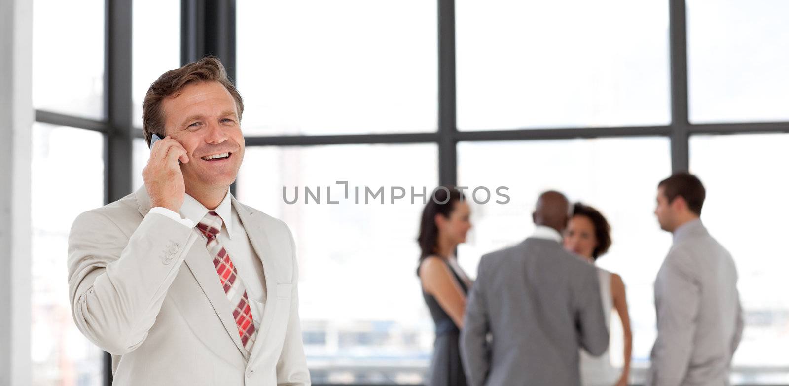 Portrait of a smiling businessman on phone with his team in the background