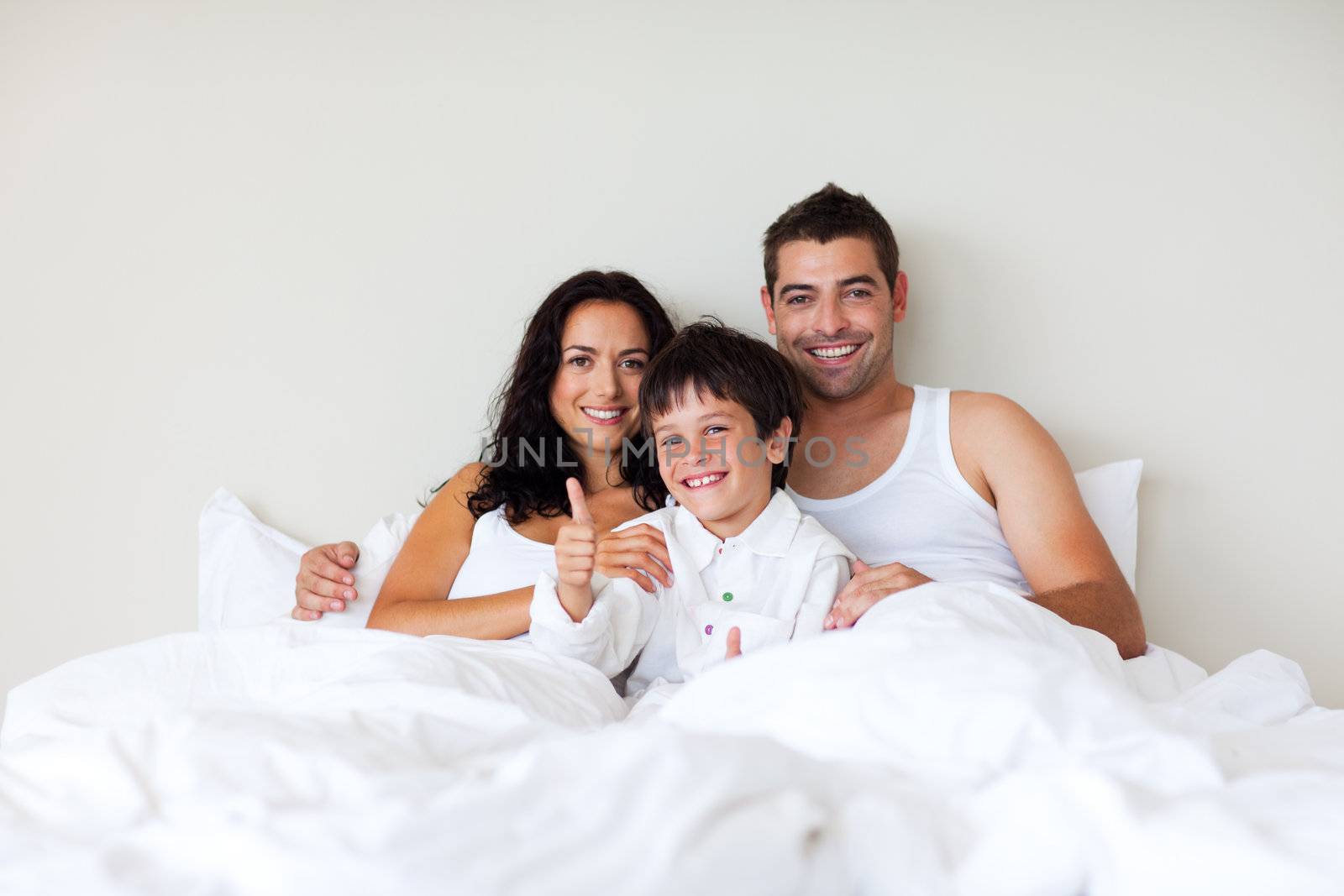 Child with thumbs up and his parents in bed by Wavebreakmedia