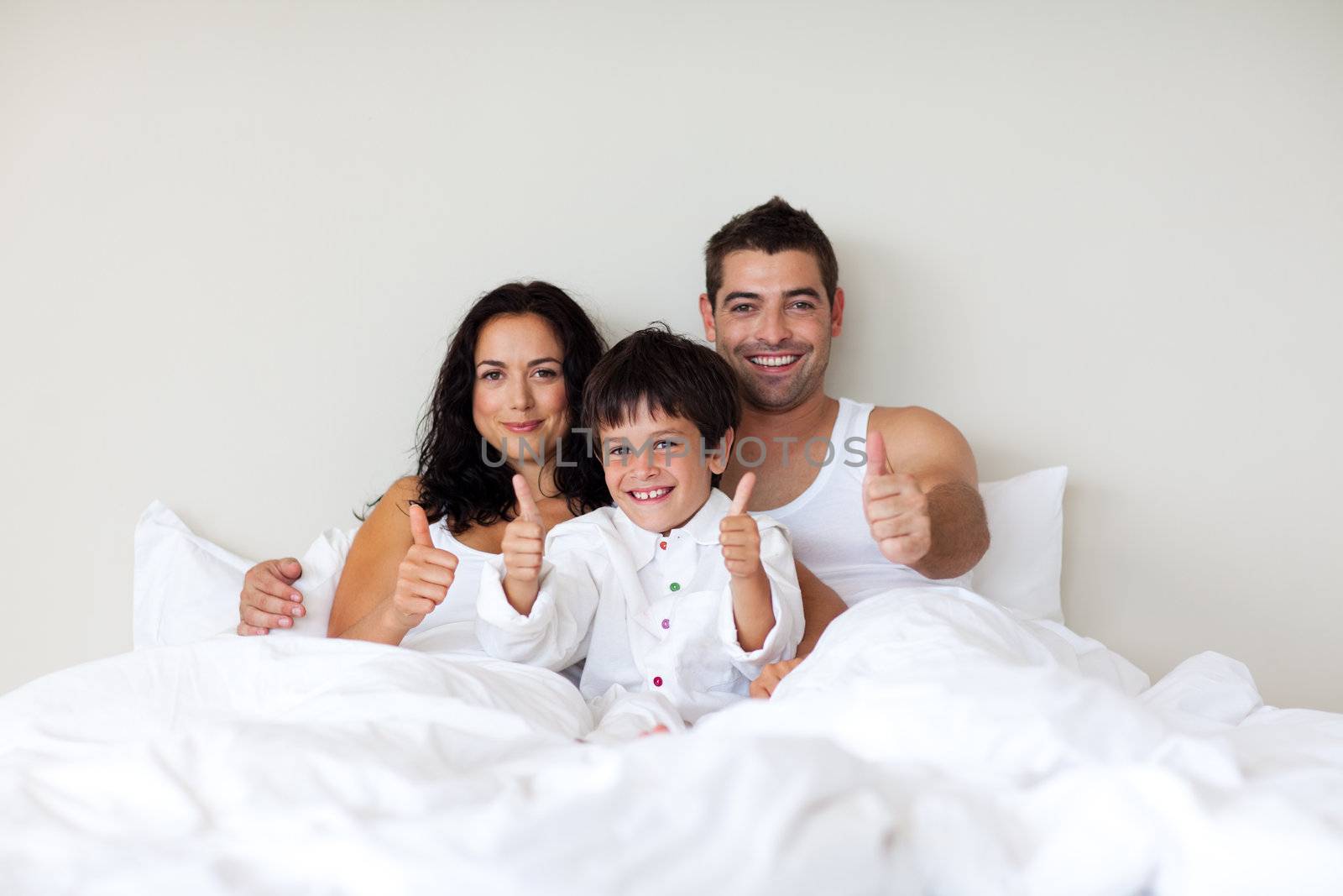 Smiling little boy with thumbs up and his parents in bed