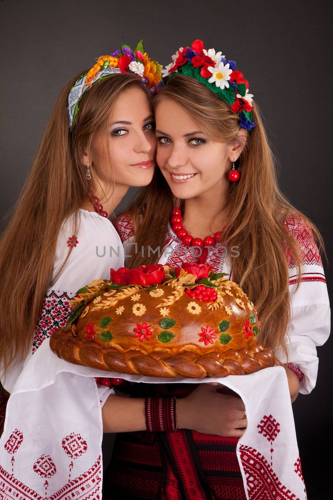 Young women in ukrainian clothes, with garland and round loaf on black background